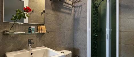 A modern bathroom with a white sink, toilet, and glass shower enclosure.