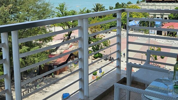 Un balcón con mobiliario de mimbre, vista a una playa y una isla distante.