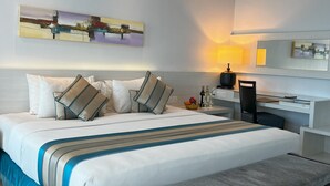 Habitación de hotel con una cama grande, un escritorio, una silla, una lámpara y una mesita con un frutero.