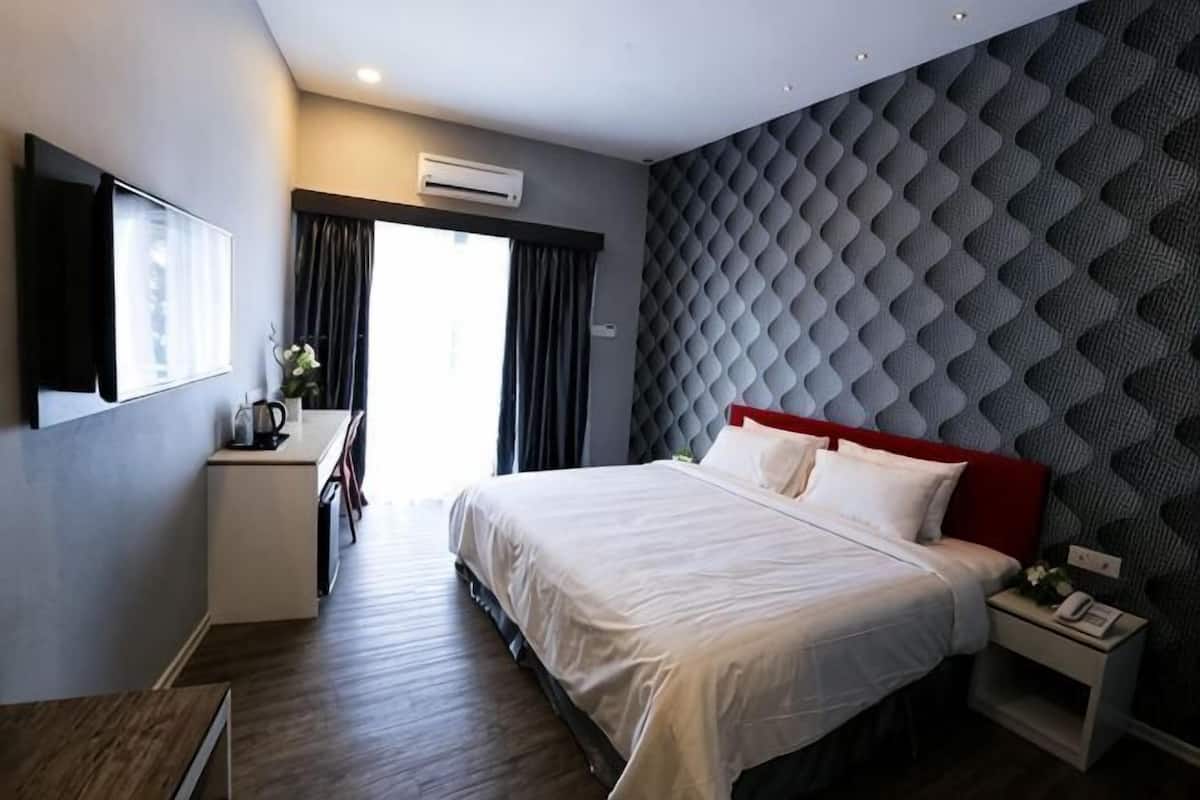 Una habitación de hotel con cama, mesita de noche, escritorio y ventana con cortinas.