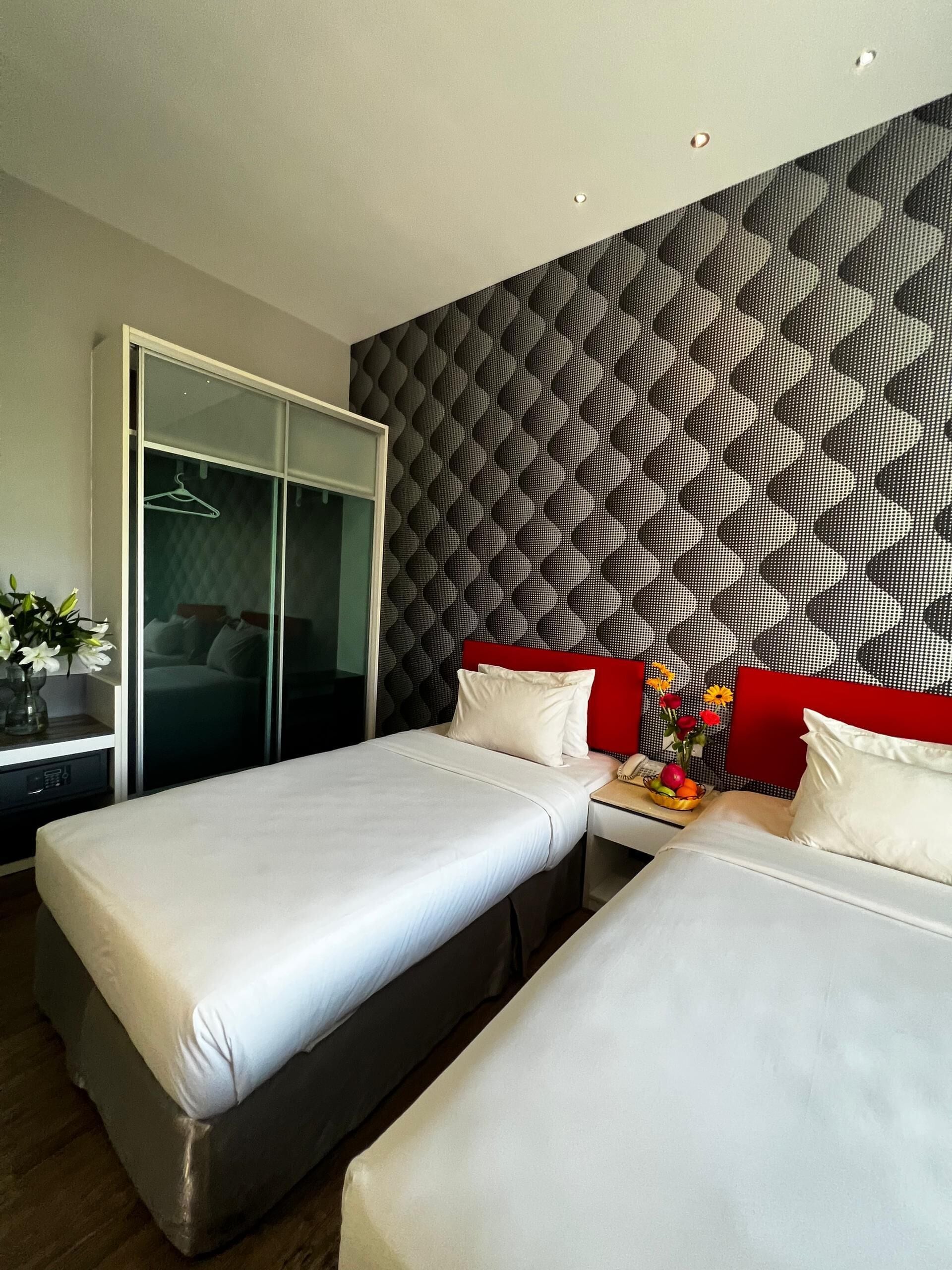 Een hotelkamer met twee bedden, een kledingkast, een bureau met een schaal fruit en een decoratief wandpaneel.