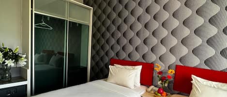 Quarto de hotel com duas camas, um guarda-roupa, uma mesa com uma cesta de frutas e um painel decorativo na parede.