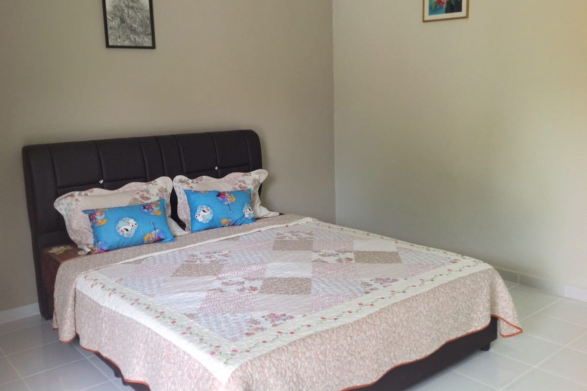 Un dormitorio con cama, dos almohadas, cabecera y pared con un cuadro enmarcado.