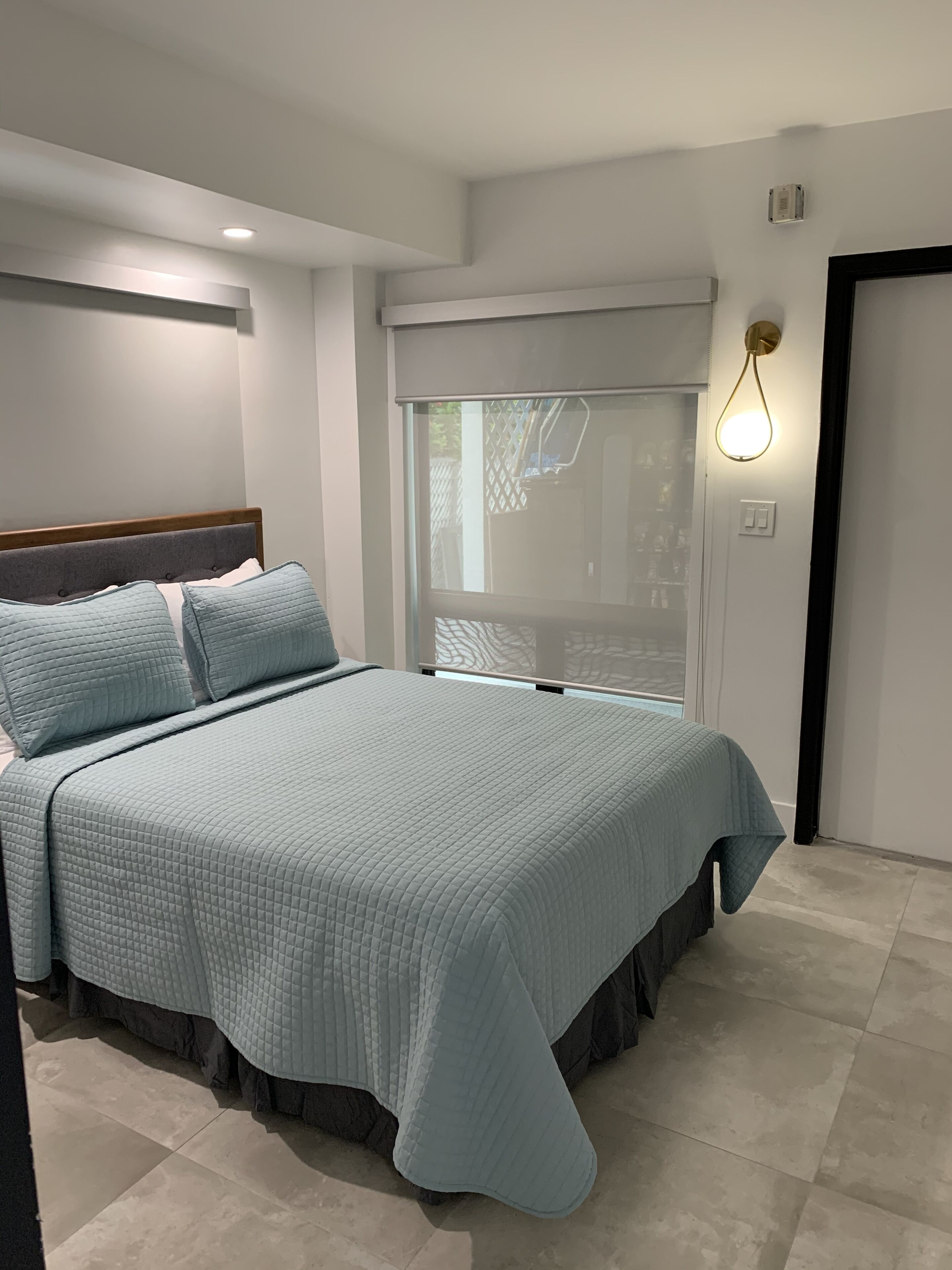 Quarto com cama, janela e luminária fixada na parede.