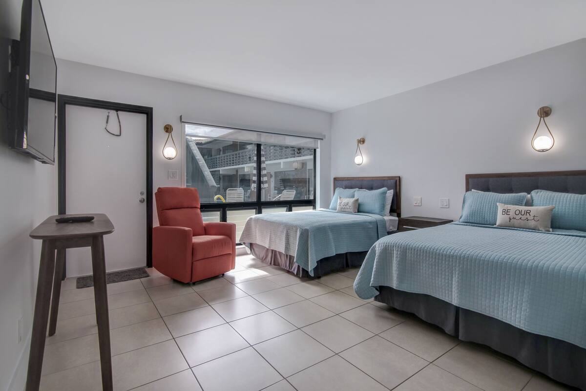 Een hotelkamer met twee bedden, een rode stoel, een tafeltje en een televisie.