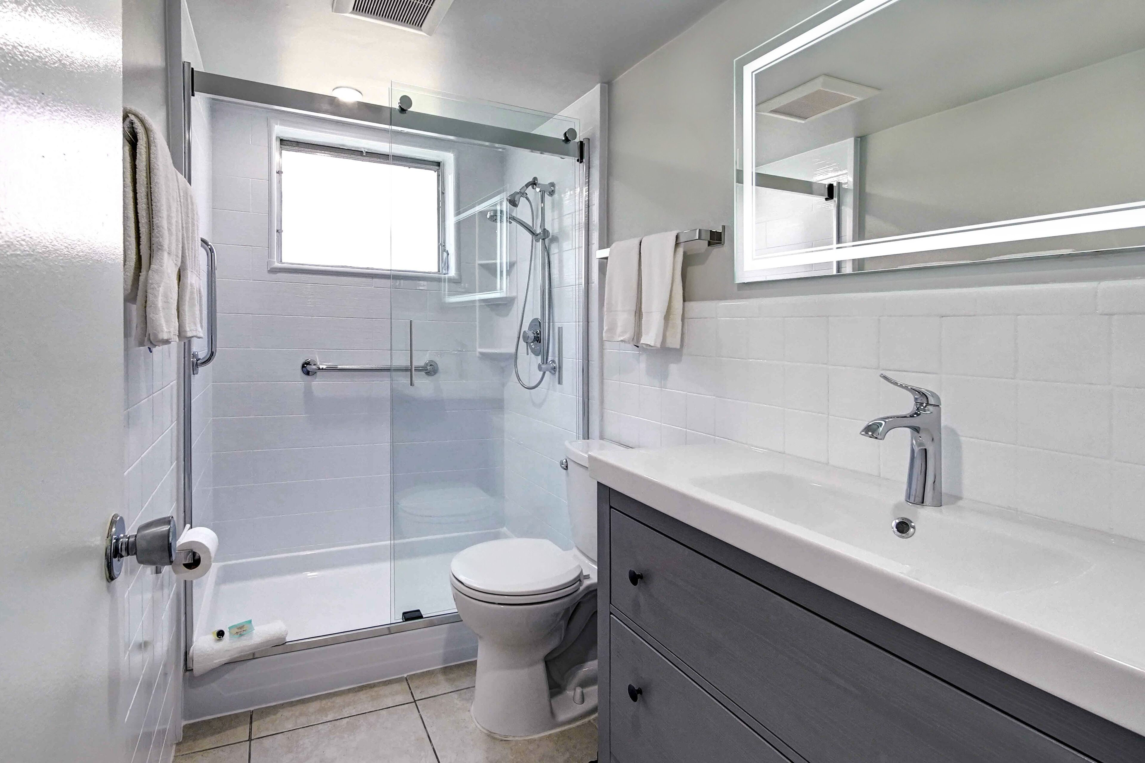 Une salle de bain moderne avec une douche à parois de verre, des toilettes, un meuble-lavabo avec un miroir et un porte-serviettes.
