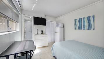 Un dormitorio con cama, escritorio, silla, ventana, lavamanos y microondas.