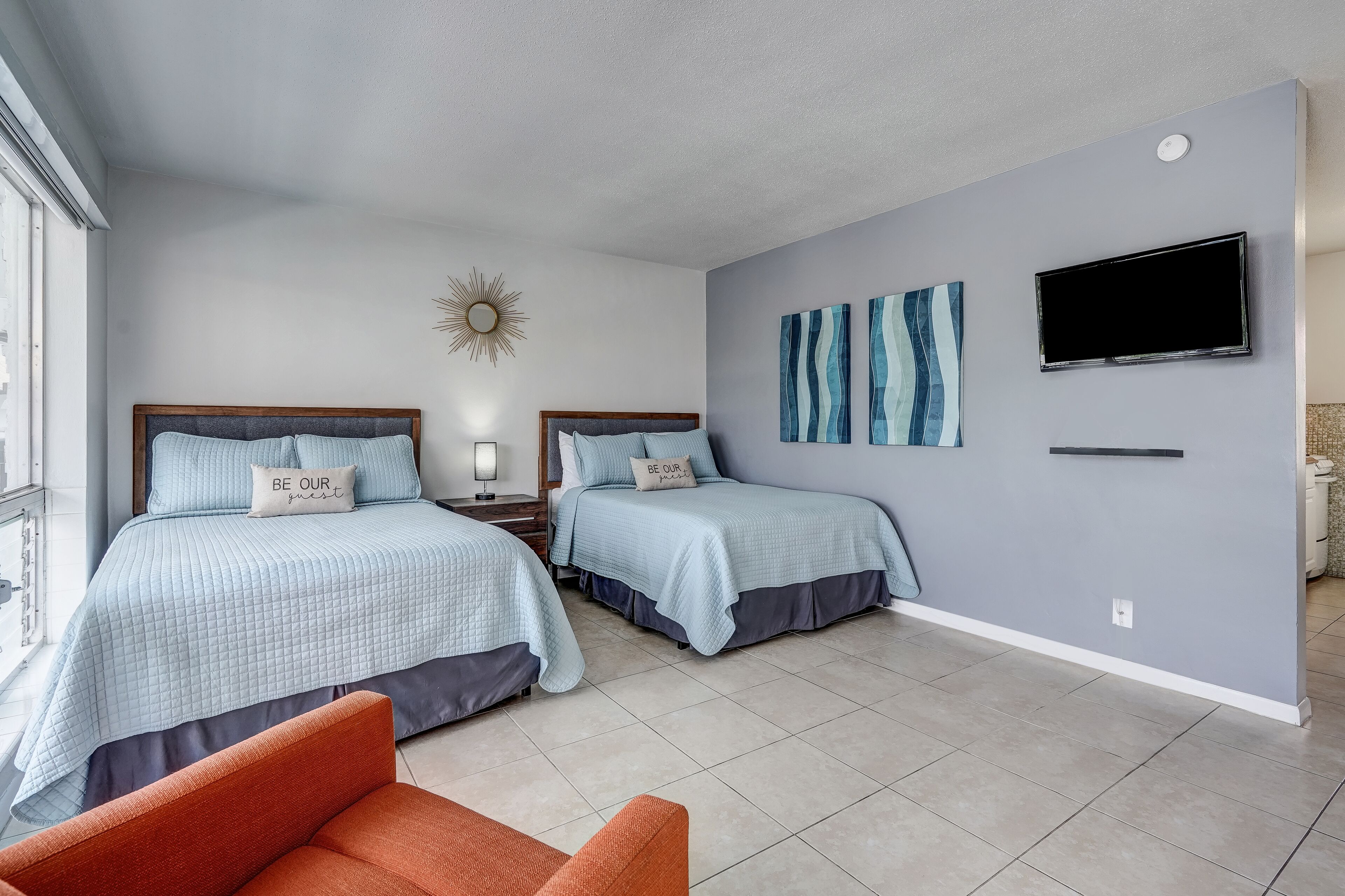 A hotel room with two beds, a TV, artwork on the wall, and a window.