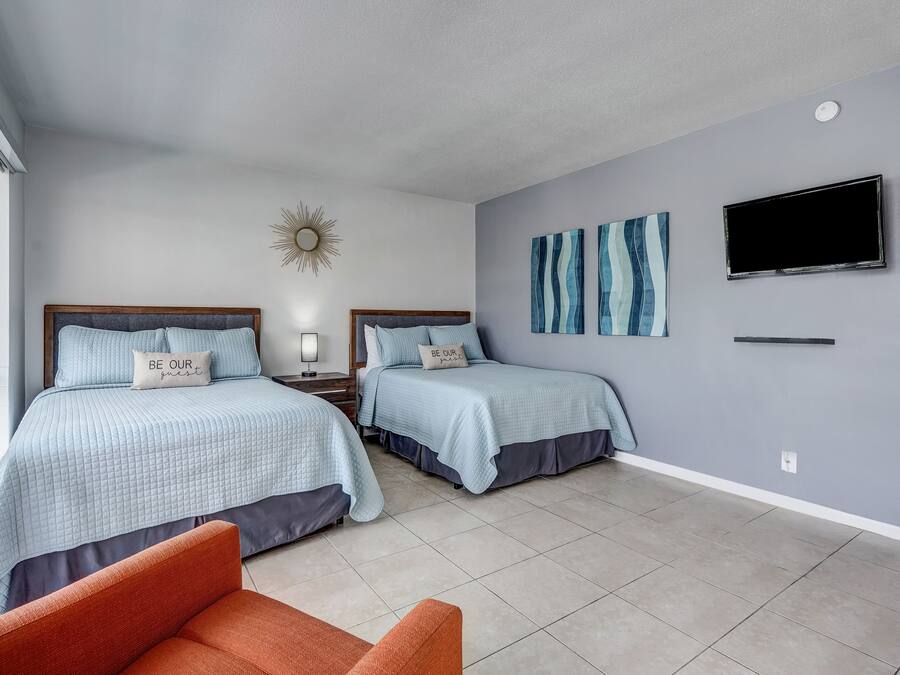 A hotel room with two beds, a TV, artwork on the wall, and a window.