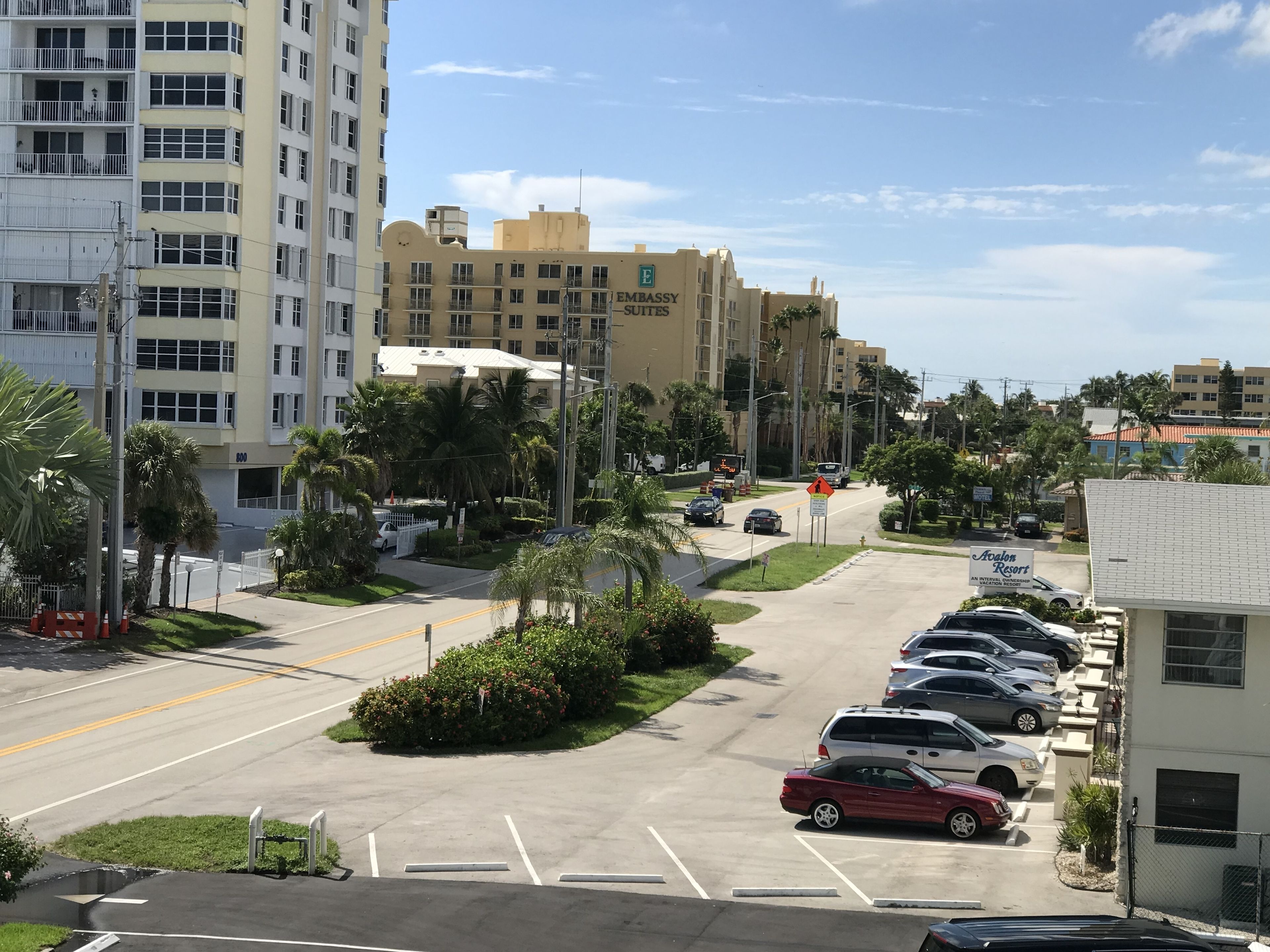 Un parking rempli de voitures, un bâtiment portant l’inscription « Embassy Suites » et un panneau indiquant « Aloha Resort ».