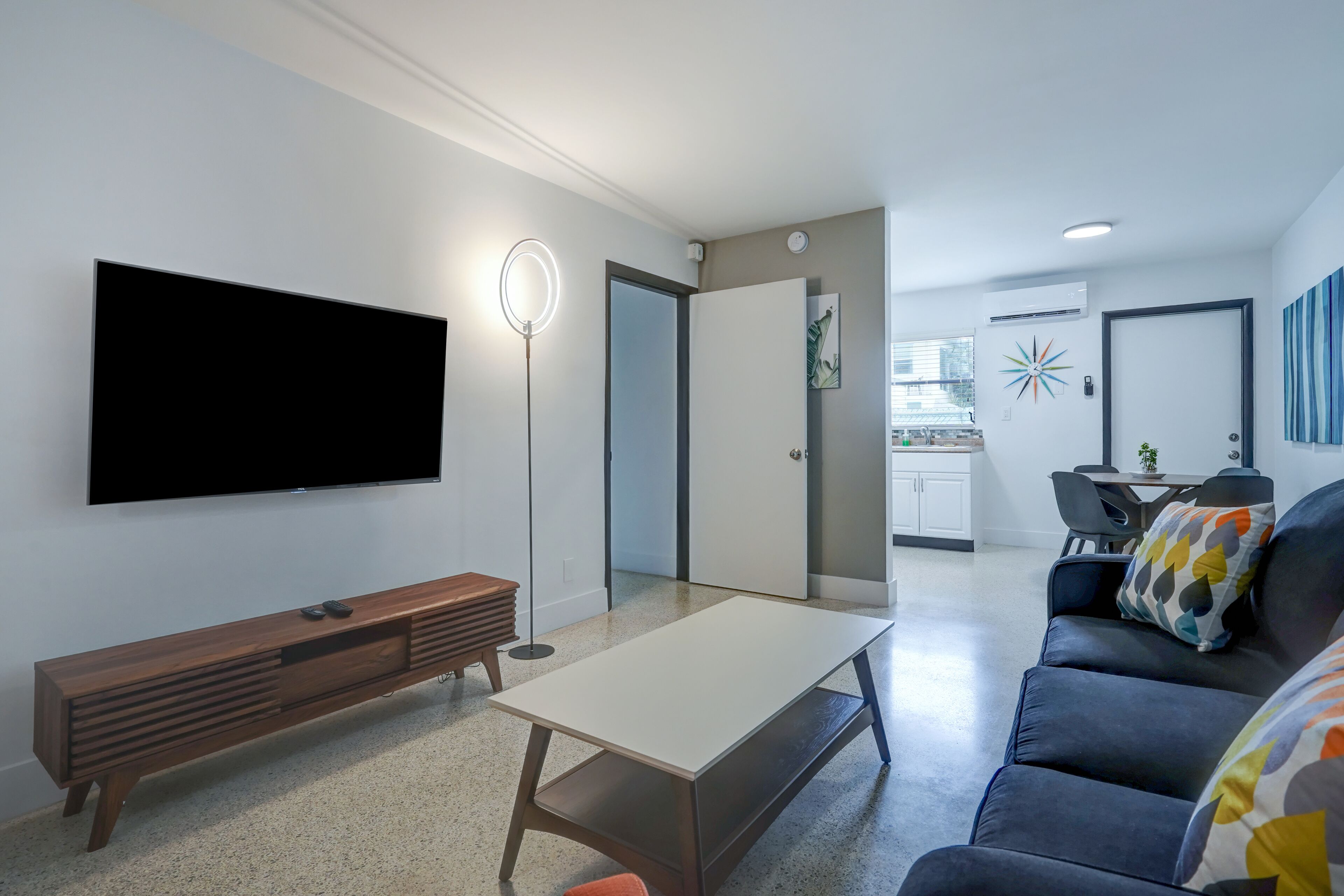 A modern living room with a flat-screen TV, a wooden entertainment unit, a coffee table, a sofa, and a ring light.