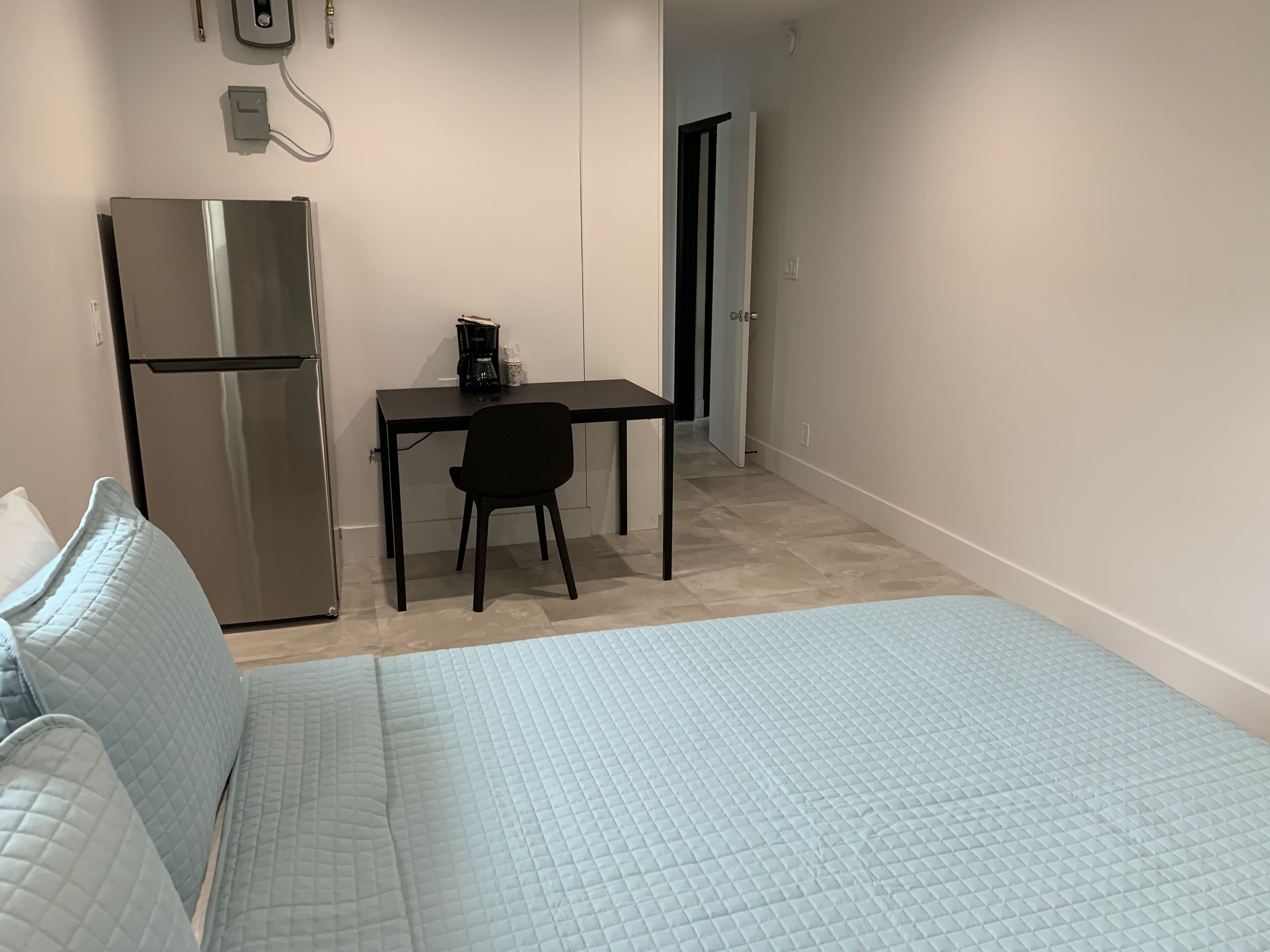 Un dormitorio con cama, escritorio y refrigerador.