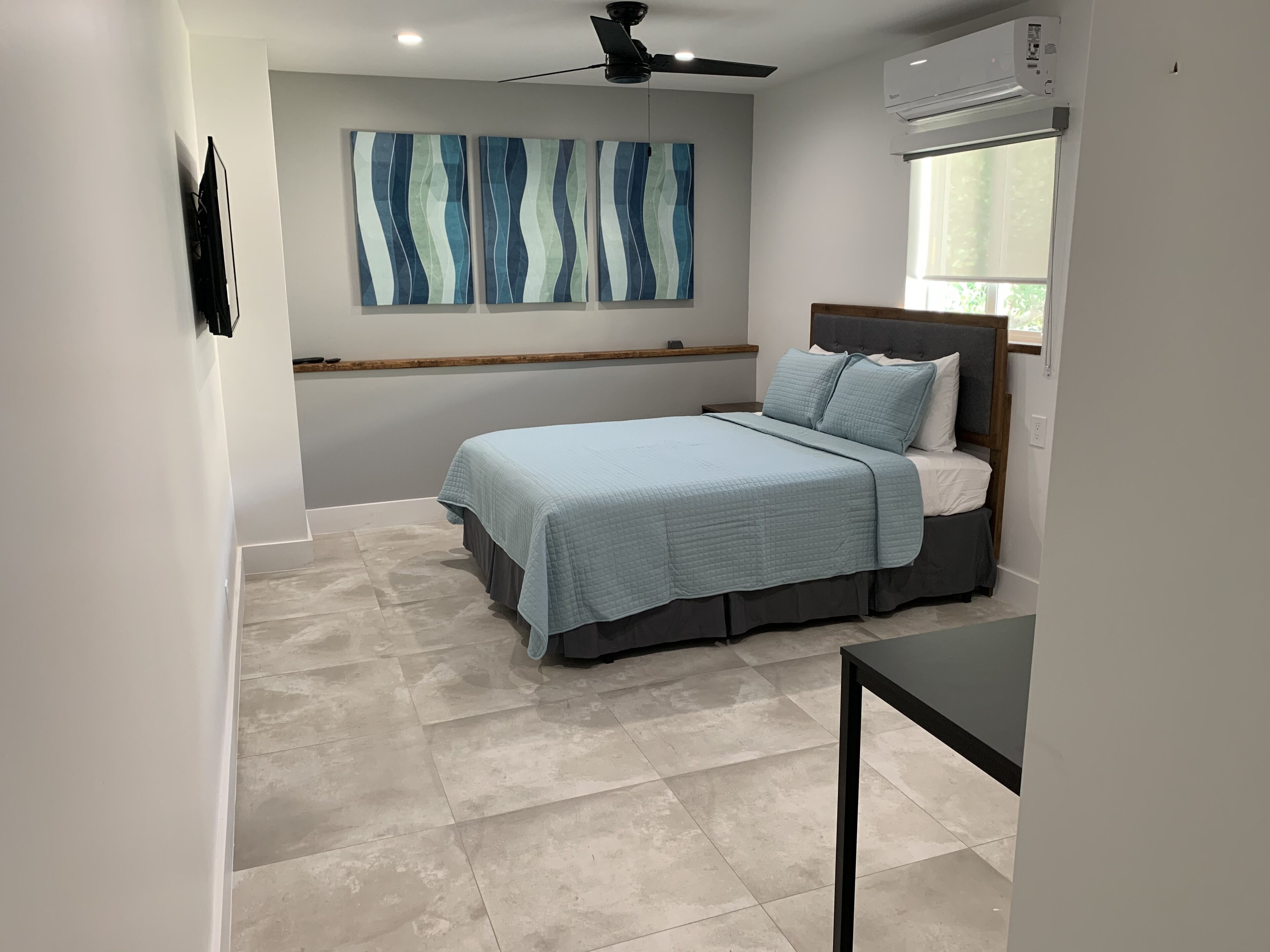 Une chambre à coucher avec un lit, un ventilateur de plafond, un appareil de climatisation et une fenêtre avec des rideaux.
