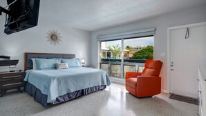 Un dormitorio con cama, mesita de noche, silla, ventana grande y puerta.