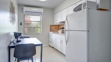 Una cocina compacta con armarios blancos, un refrigerador de acero inoxidable y una ventana con persianas.