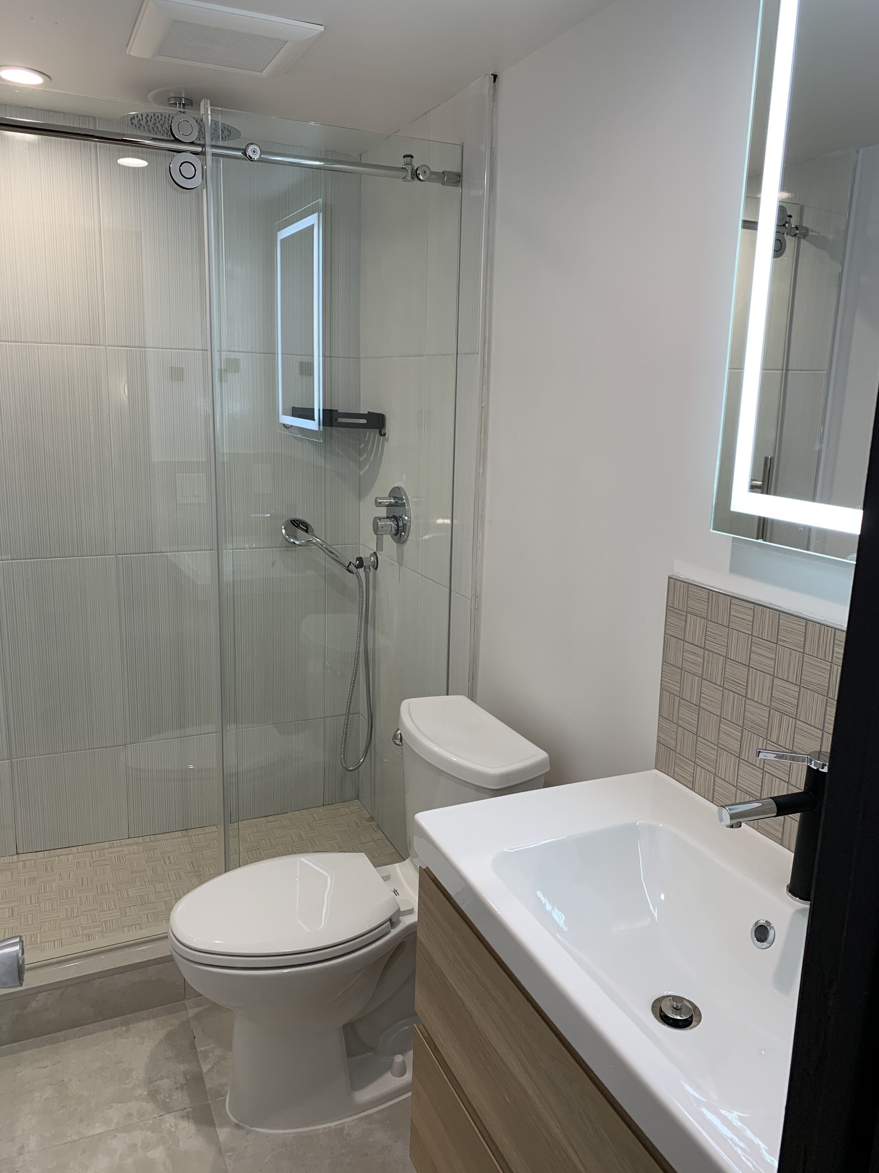 A modern bathroom with a glass-enclosed shower, a white toilet, and a large bathtub.