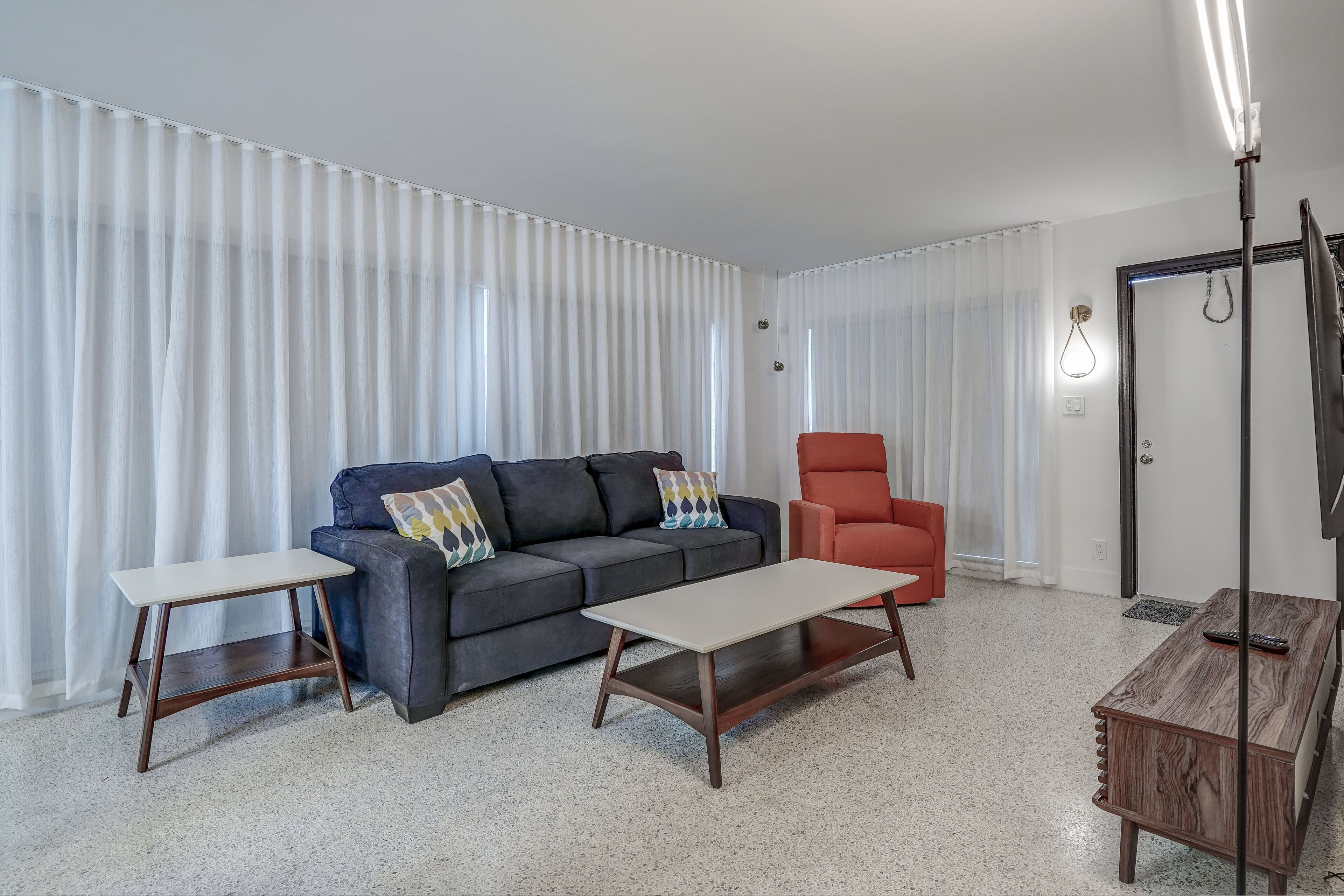 A living room with a dark grey sofa, a red armchair, a white coffee table, and a small white side table.