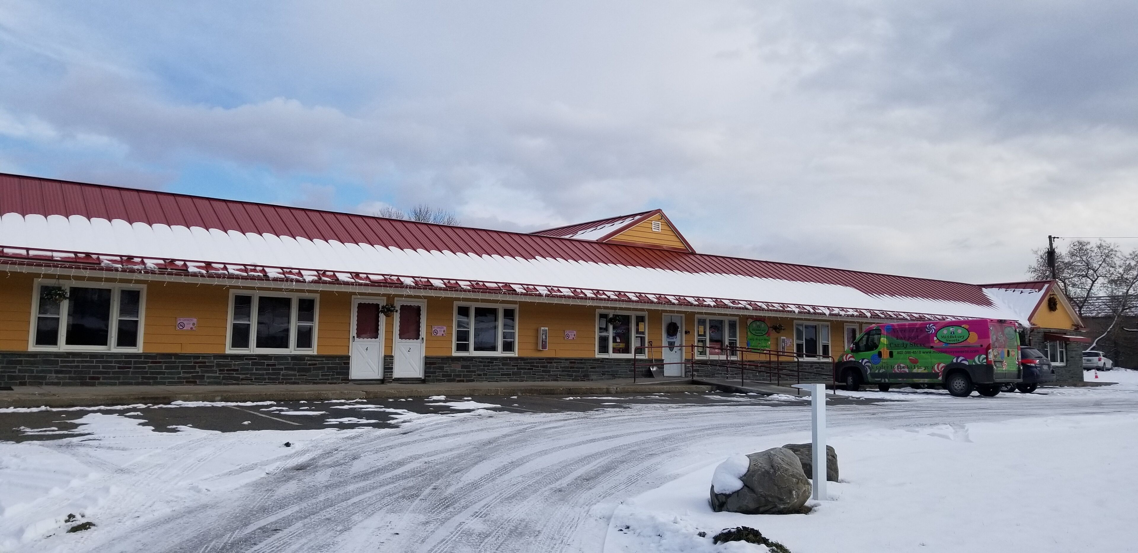 A yellow building with a red roof, a parked colorful food truck, and snow on the ground.
