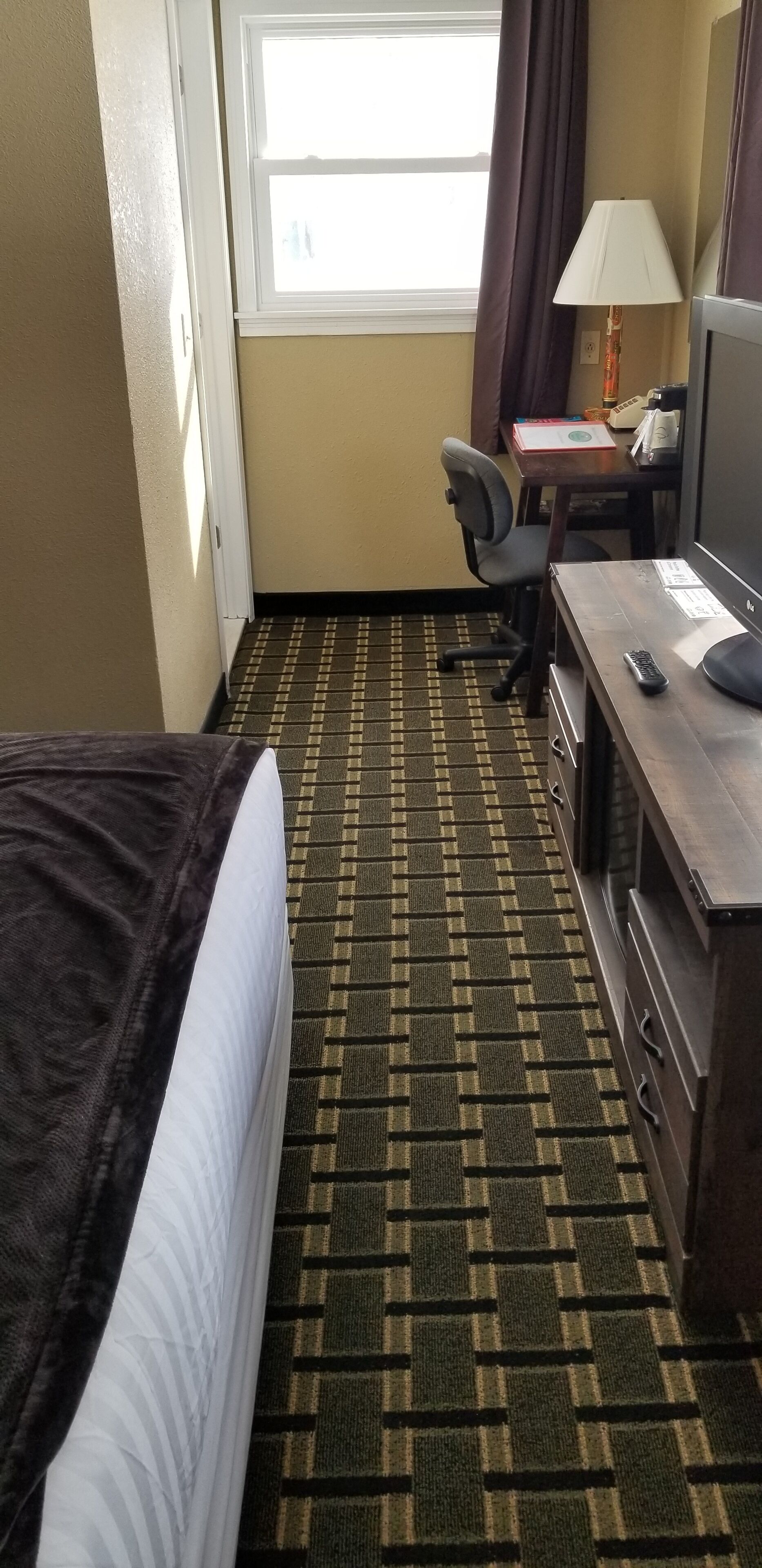 A hotel room with a bed, a desk, a chair, a lamp, and a television.
