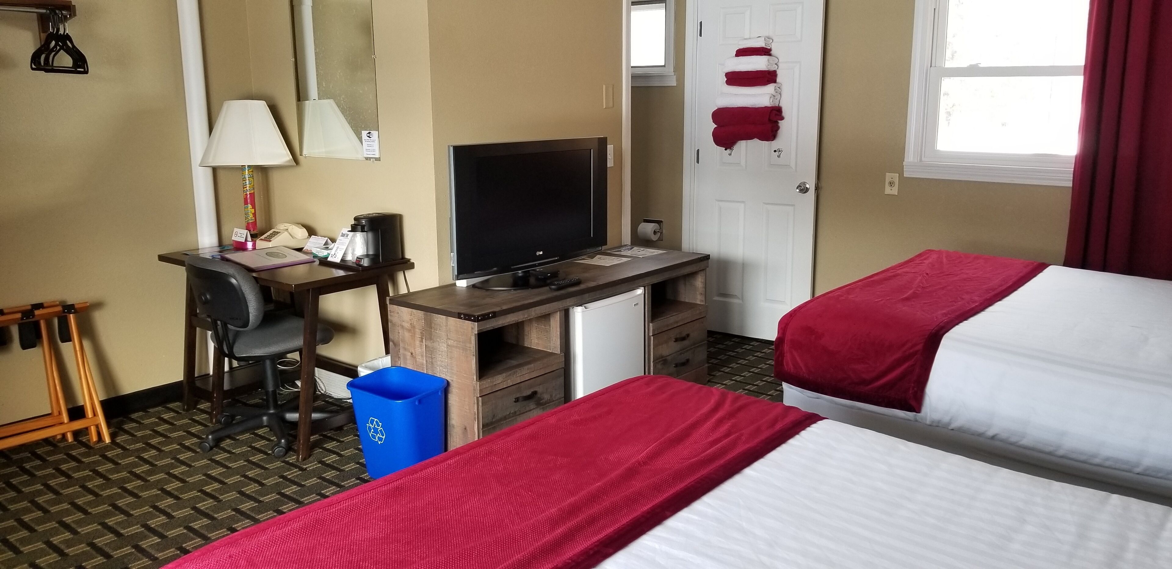A hotel room with a desk, computer, and two beds with red and white bedding.