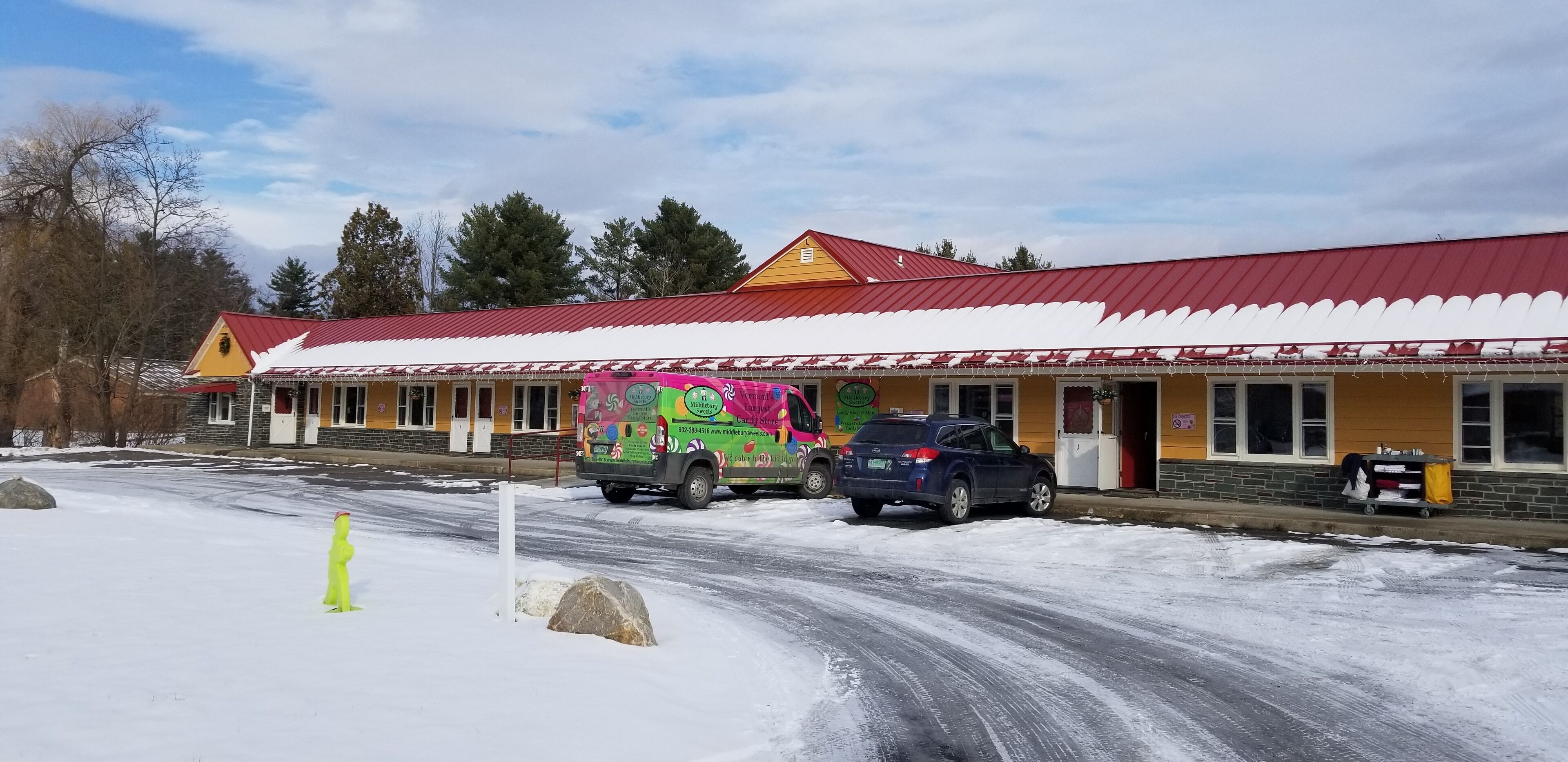 A building with a red roof and yellow walls, featuring a colorful van parked in front.