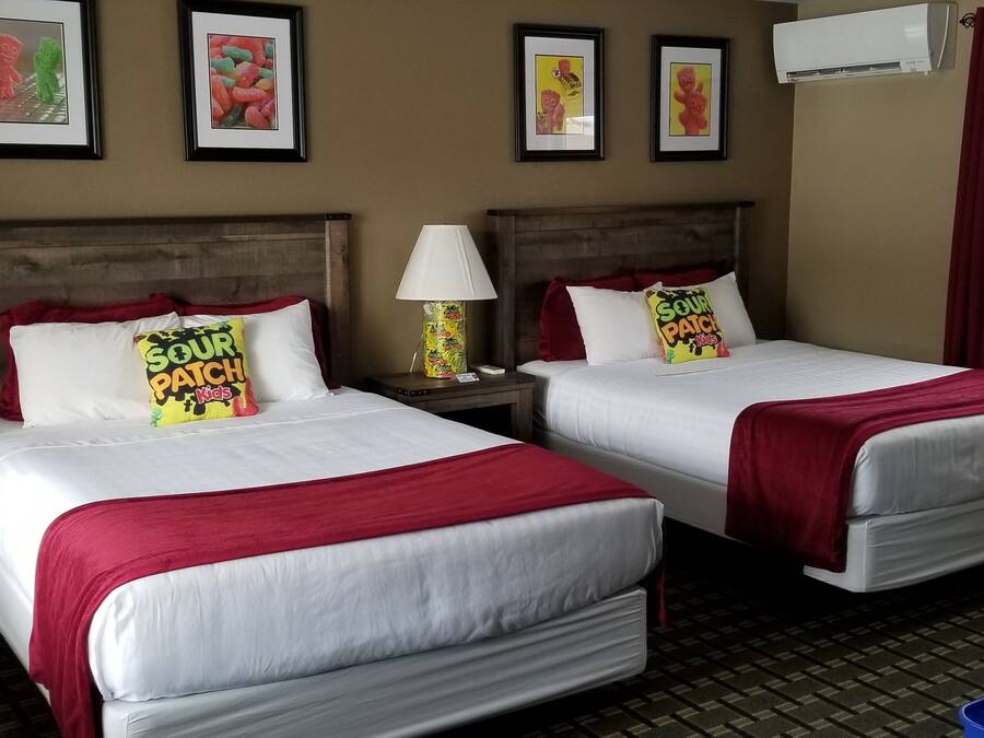 A hotel room with two beds, each with white bedding and red accents, a television on a wooden stand, and a window with red curtains.