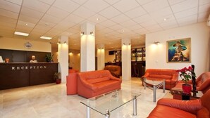 A reception area with a reception desk, two orange sofas, a glass coffee table, and a painting on the wall.