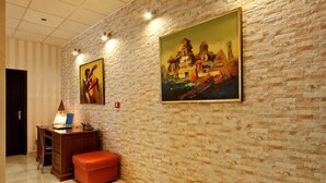 A room with a brick wall, a desk with a lamp, and two paintings.