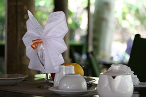 A dining table with a white napkin tied in a bow, salt and pepper shakers, a glass, and a plate with a lemon. - Jump Street Chalets (Maun)