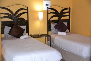 Two single beds with headboards, a bedside table with a lamp, and a wall-mounted light switch. - Jump Street Chalets (Maun)