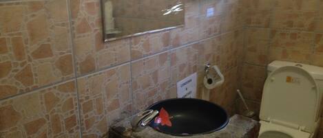 A bathroom with stone tiles, a toilet, a sink with a black basin, and a mirror.