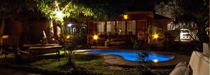 Une vue nocturne d’une cour arrière avec une piscine, du mobilier d’extérieur et un bâtiment doté de grandes fenêtres.