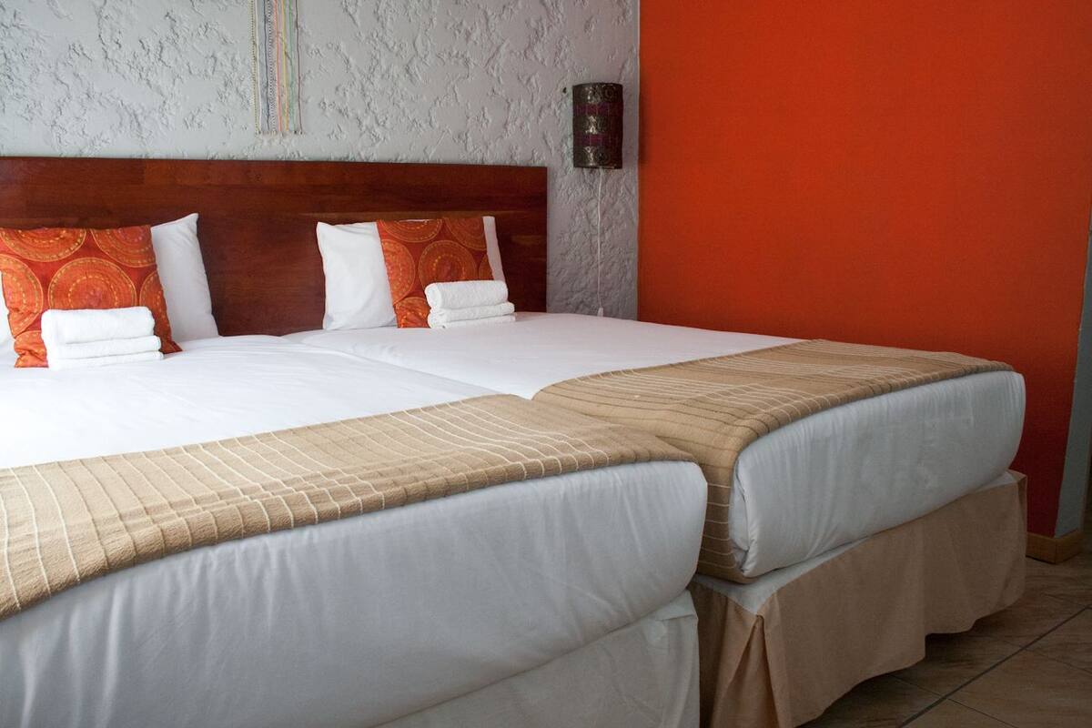 A double bed with white and beige bedding, a wooden headboard, and orange patterned pillows.