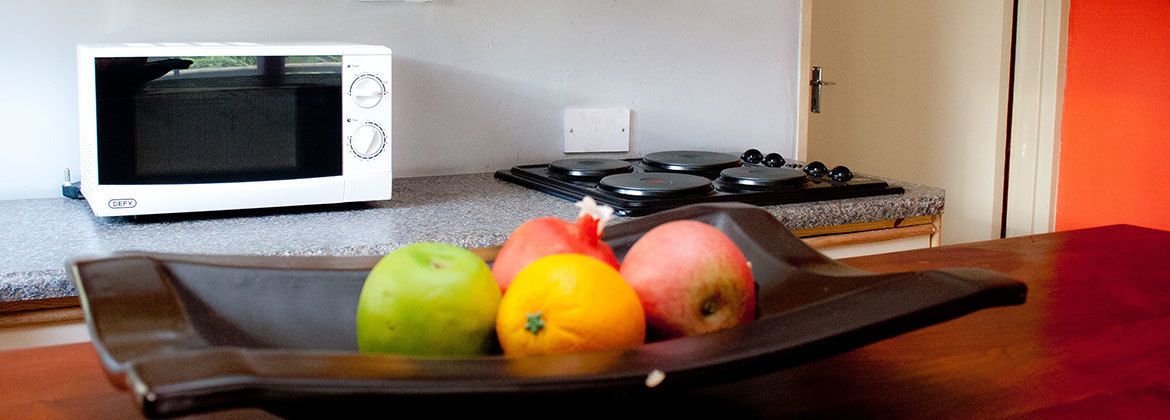 A kitchen with a microwave, stove, and a tray with fruits.