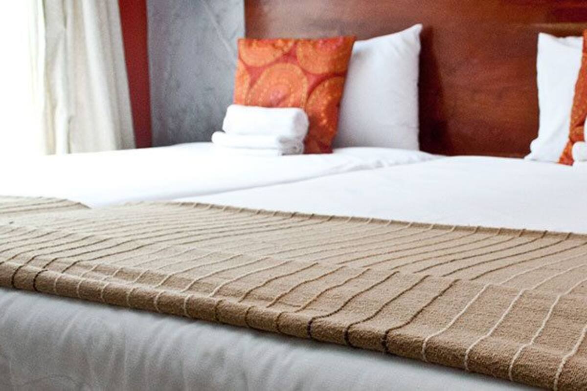A double bed with a brown textured bedspread, white linens, and orange patterned pillows.