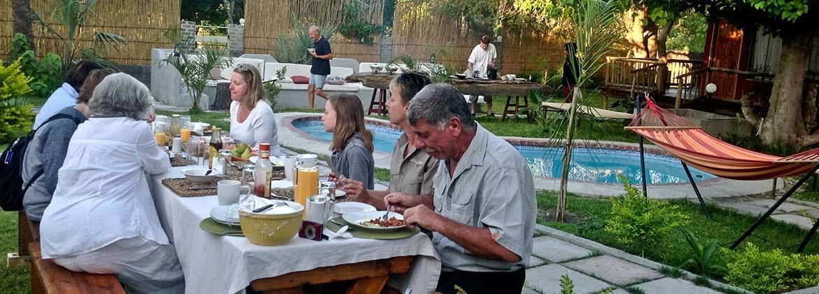 Un groupe de personnes est assis à une table en plein air et prend son repas, avec une piscine en arrière-plan.