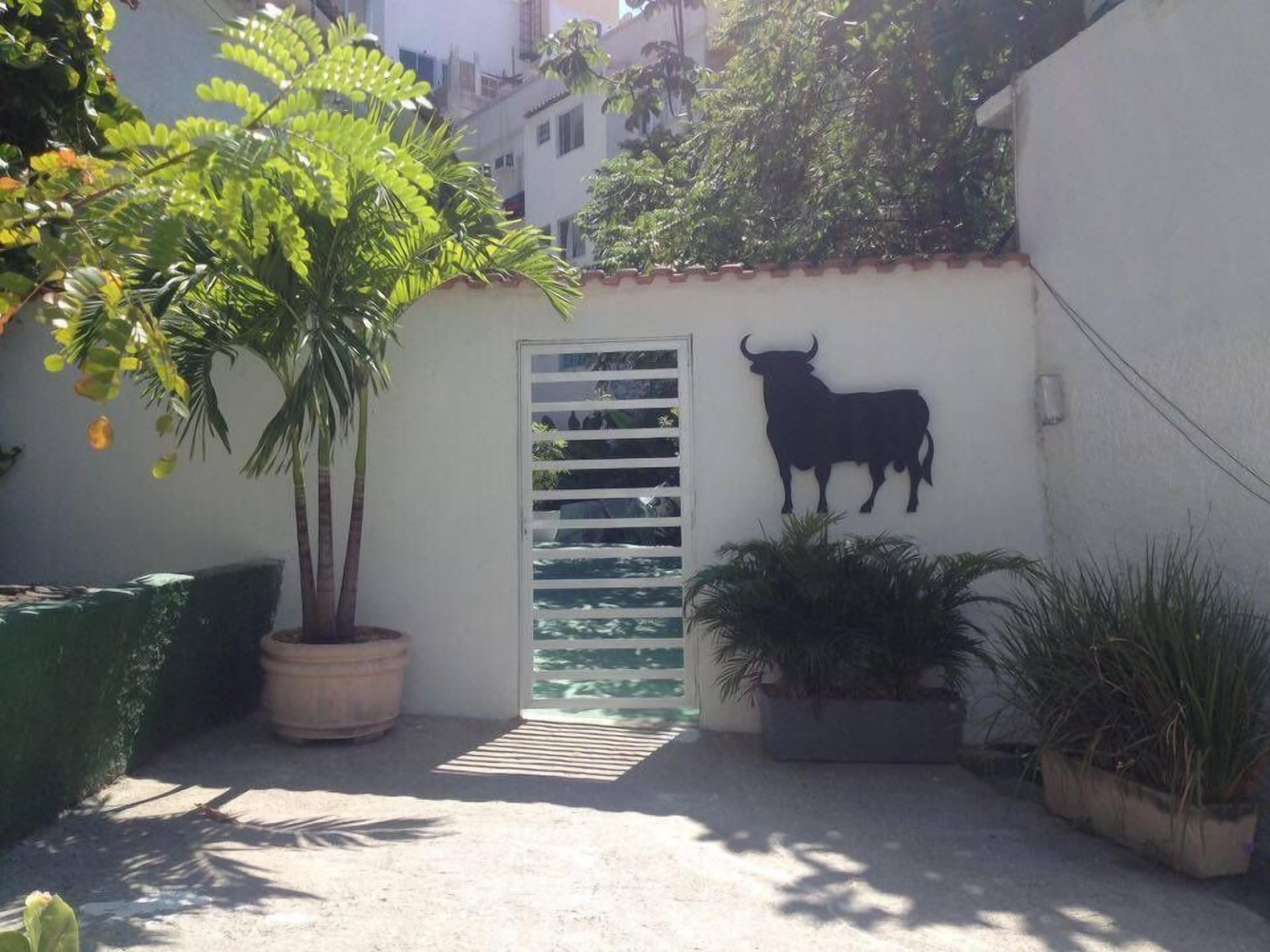 A courtyard with a white wall, a bull silhouette, and potted plants.