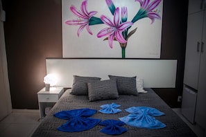 A bedroom with a bed, pillows, a nightstand, a lamp, and a painting of flowers on the wall. - Casa del Angel (Rio de Janeiro)
