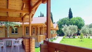 A wooden cabin with a covered patio area, outdoor seating, and a well-maintained garden. - Sandy's Studios Apartments & Log Villas (Kos)