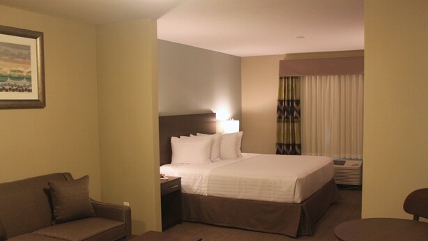 Een hotelkamer met een bed, nachtkastje, lamp, bank, een klein rond tafeltje en een raam met gordijnen.