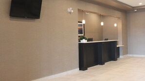 Een receptiegedeelte met een wandgemonteerde flatscreen televisie, een receptiebalie en hanglampen.