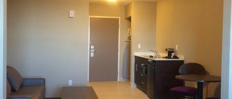 Un espacio habitable compacto con kitchenette, un sofá, una pequeña mesa y una silla.