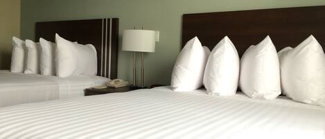 Una habitación de hotel con dos camas, ropa de cama blanca, una mesita de noche con lámpara y teléfono.