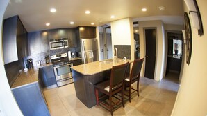 A modern kitchen with dark cabinetry, stainless steel appliances, and a central island with bar stools. - Corporate Suites of Calgary - Eightwelve (Calgary)