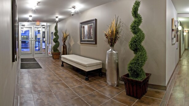 A hallway with a bench, a door marked 'EXIT', and two potted plants. - Corporate Suites of Calgary - Eightwelve (Calgary)