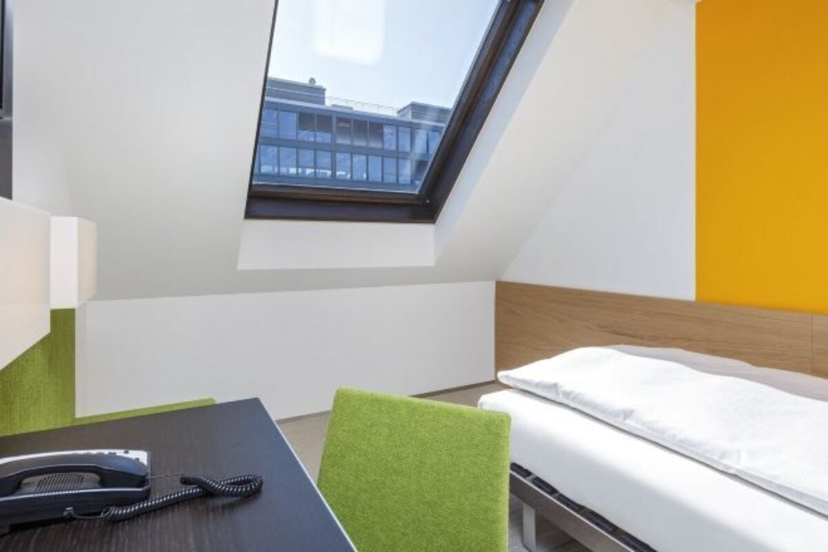 Habitación de hotel con tragaluz, una cama, un escritorio con teléfono y una silla verde.