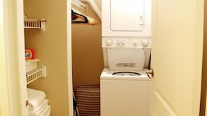 Une petite buanderie comprenant un lave-linge, un étendoir et une étagère avec des serviettes pliées.