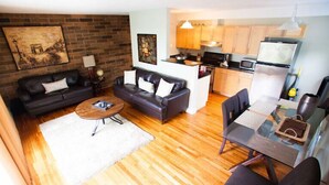 Un espace de vie compact comprenant un canapé, une table basse, une table à manger avec des chaises, un coin cuisine avec des meubles en bois et des appareils modernes.
