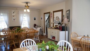 A dining area with wooden tables and chairs, a chandelier, and a kitchen in the background. - Candlebay Inn (Freeport)