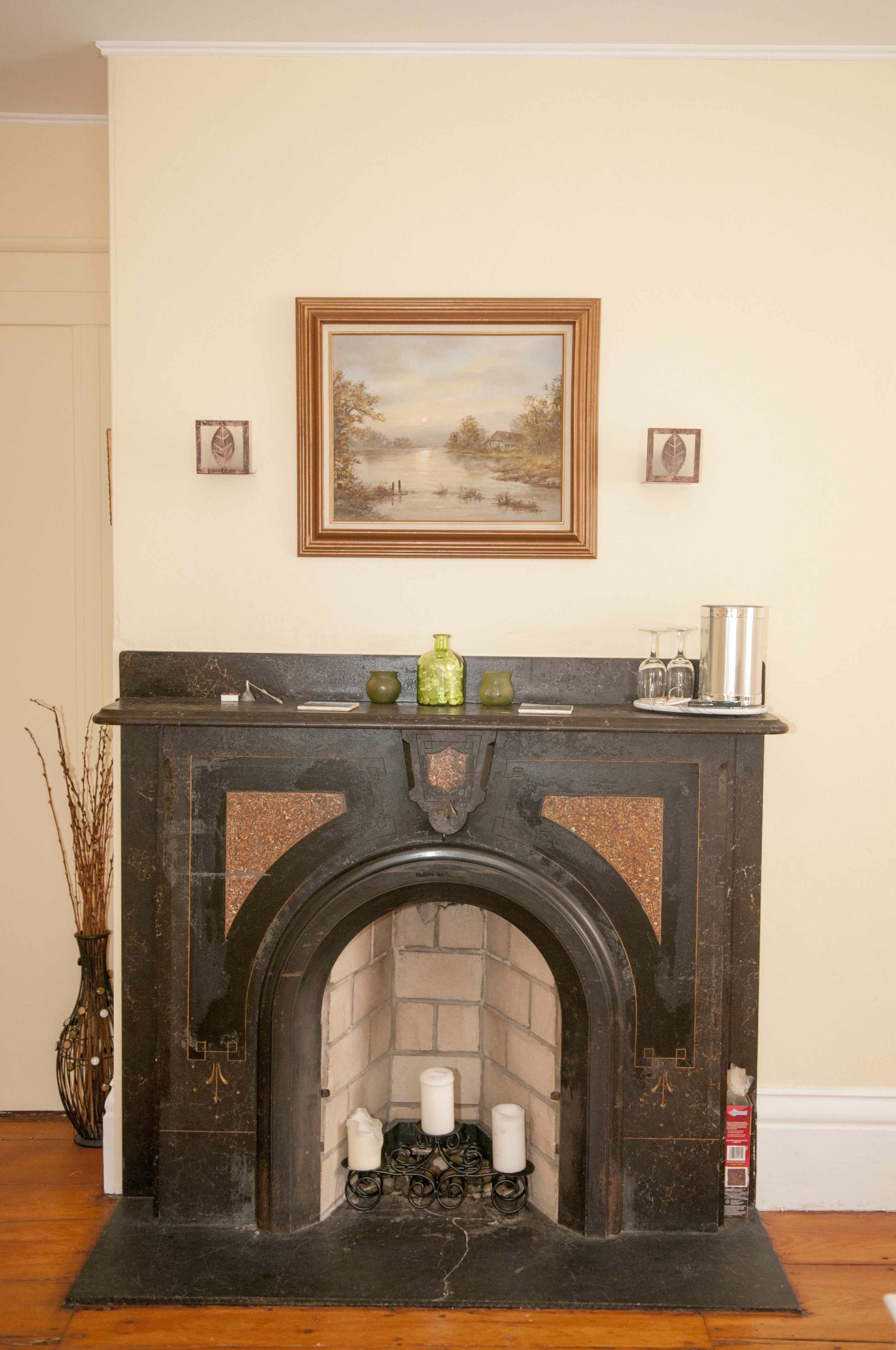 A fireplace with a mantel, a framed painting above it, and a vase on the mantel.